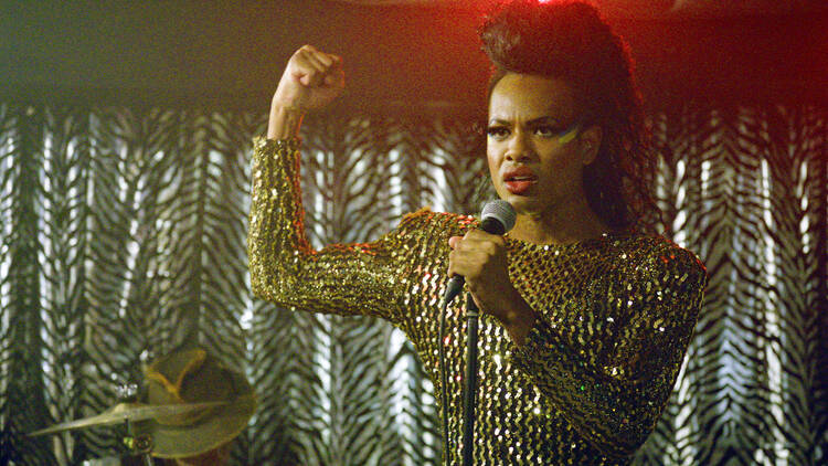 A performer in a glittery gold dress stands on stage with a microphone.