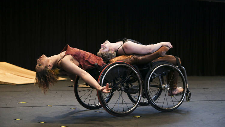 Alice Sheppard and Laurel Lawson lay backwards in their wheelchairs, torsos and throats open. Alice is a multiracial Blac k woman with coffee - colored skin and short curly hair, and Laurel is a white woman with cropped blonde hair.
