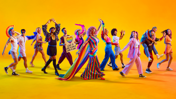 People walk in bright coloured pride clothes on a yellow background
