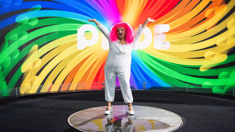 A drag queen in front of a pride sign