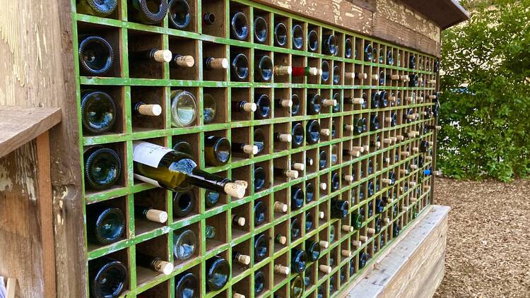 A series of wooden cubbies hold wine bottles stored horizontally, some facing in and some facing out. One bottle has been pulled out halfway.