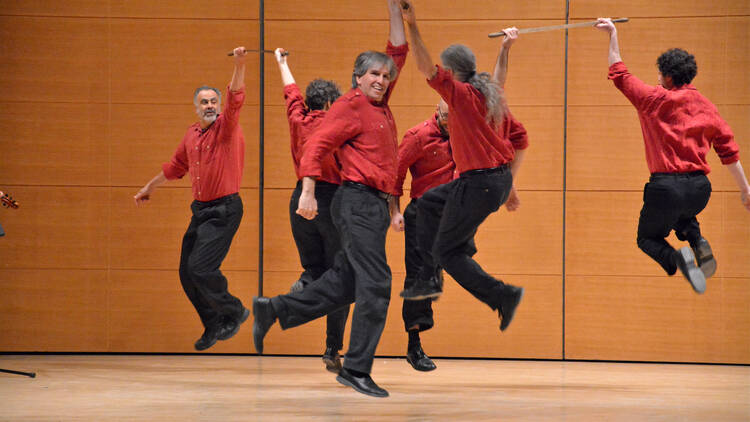 Six performers in leap on a stage as part of the New York Sword Dance Festival 