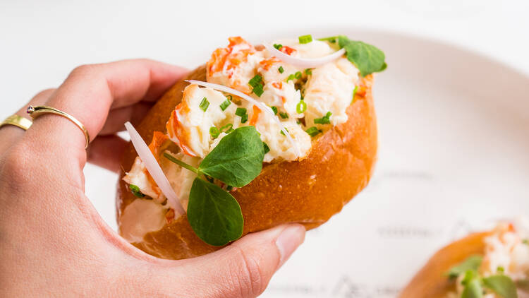 A person holds a lobster roll topped with chives and watercress.