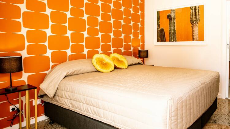 A queen-sized bed in a room with vibrant orange wallpaper.