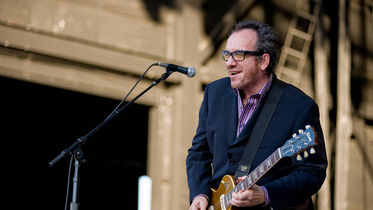 Singer Elvis Costello on stage with a guitar.