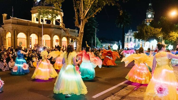 People in illuminated dresses parade down a main Bendigo street in the dark.