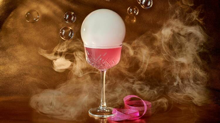 A pink cocktail with a bubble on top that's filled with smoke.