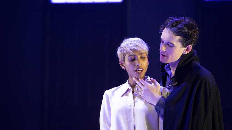 A man looms over a woman on stage and tilts her chin towards his.