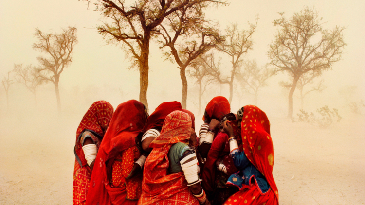 A group of women in red gather in a dust storm in India