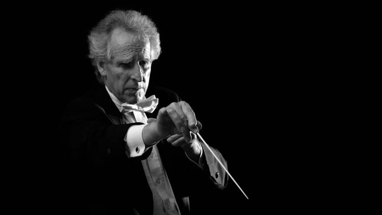 Conductor Benjamin Zander wears a tux while holding a conductor's wand.