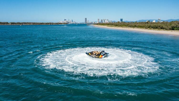 A Paradise Jet Boating vessel spins in a circle with the Gold Coast in the distance