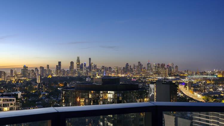 Looking out from a rooftop bar you can see the Melbourne skyline with the sun setting behind it 