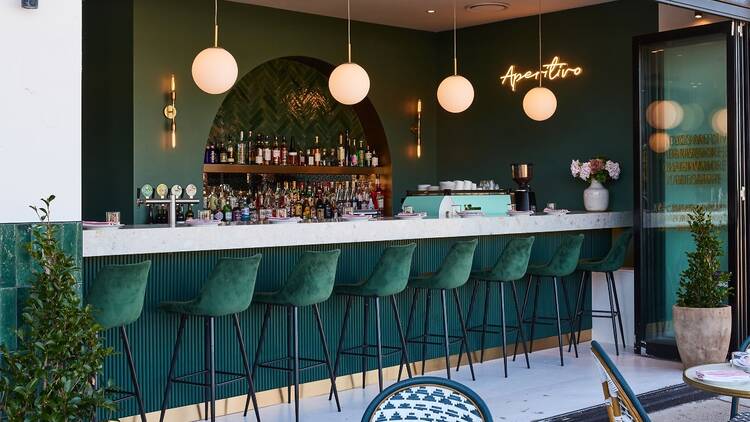 A chic green bar at Barmilano with velvet seats and hanging lights