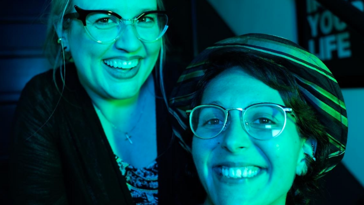 Two women pose together bathed in blue light.