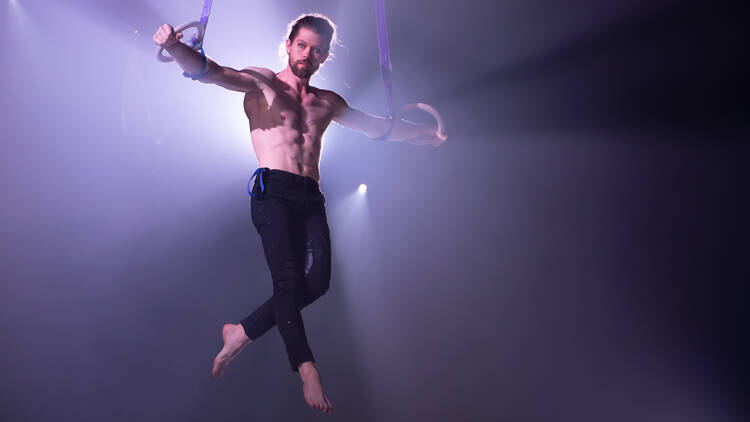 A male gymnast hangs from two rings, holding himself in a T shape.