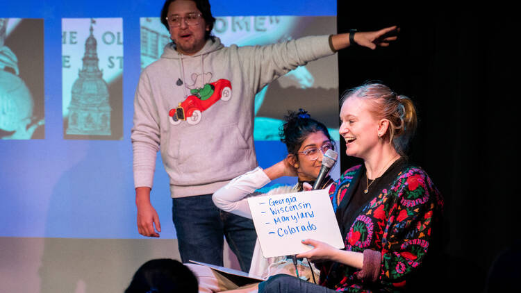 Several performers on stage, one holding a whiteboard with state names written on it.