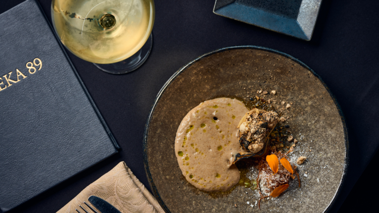 A mushroom dish and a glass of white wine on a table next to a menu.