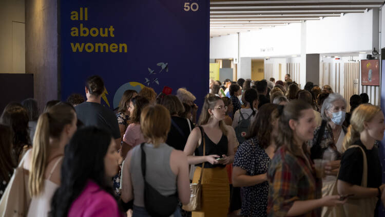 Women walking at an event, with an ALL ABOUT WOMEN sign behind them.