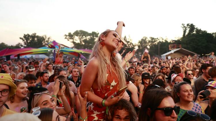 A woman with long blonde hair in a floral dress sits on someone's shoulders in the crowd at Bassinthegrass.