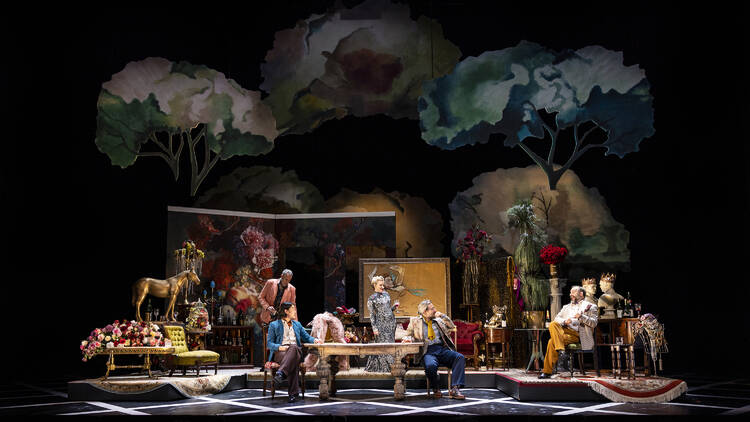 A lavish stage set with people positioned around a central table.