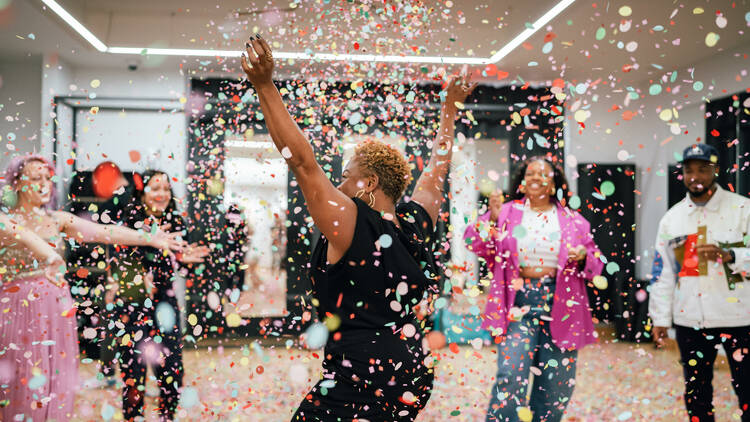 A group of five people dance around in confetti.