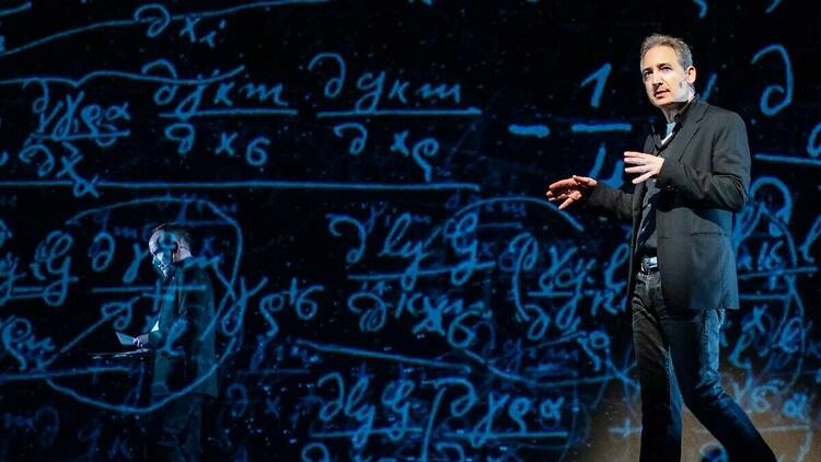 Professor Brian Greene stands in front of a board showing equations.