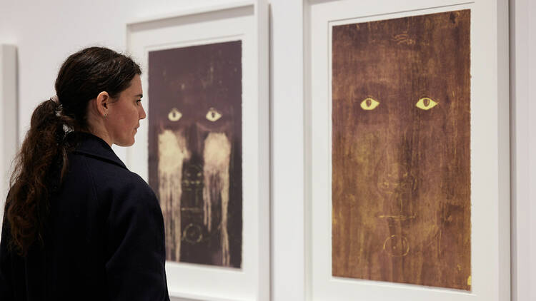 A woman looks at two paintings of faces.