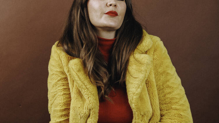 A portrait of Sara Hennessey wearing a fluffy yellow coat. 