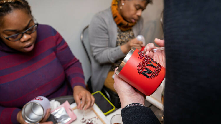 People apply rhinestones to stainless mugs.