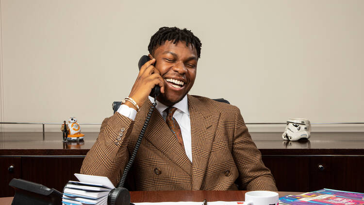 Actor John Boyega sitting at a desk laughing on phone