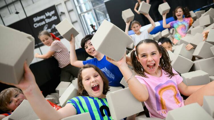 Kids in a foam pit smile and hold up pieces.