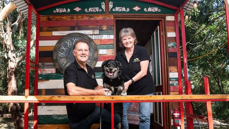 A middle aged couple and a dog outside a 'gypsy' caravan