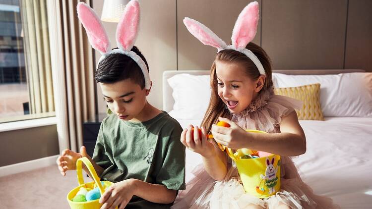 Two kids wearing rabbit ears in a hotel suite with Easter eggs