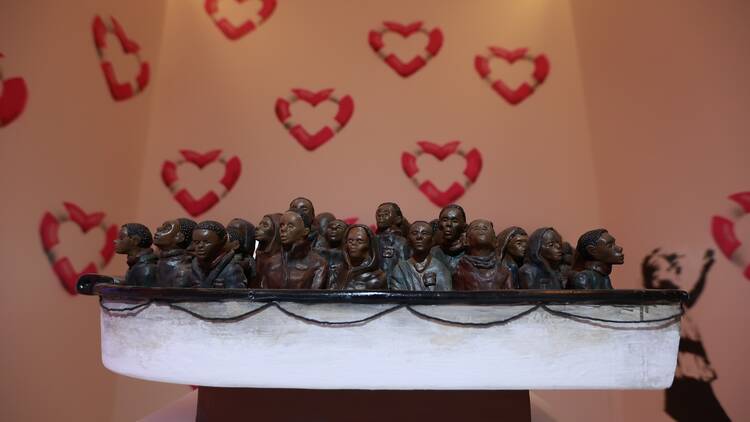 A sculpture featuring small ceramic people in boat, with heart-shaped lifebuoys