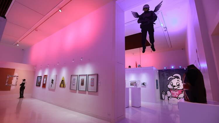 A purple-lit gallery space featuring artworks by Banksy.
