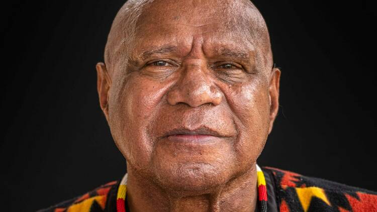 Close-up of Archie Roach looking straight at the camera, with a black background.