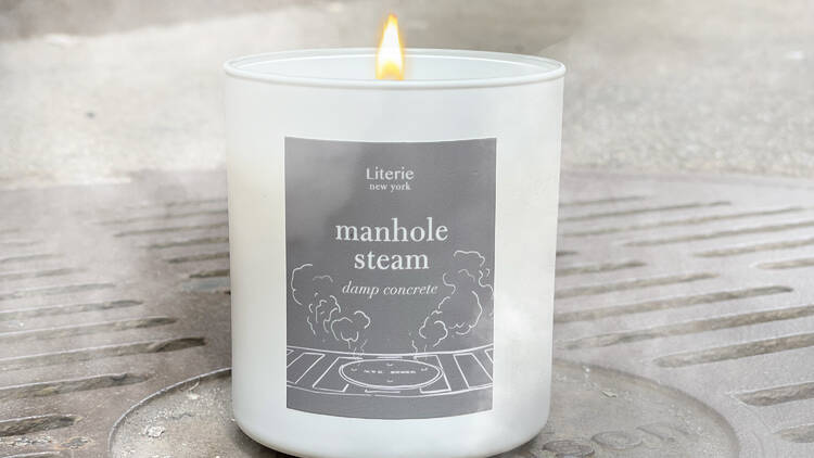 A "Manhole Steam" scented candle sits on a manhole with steam.