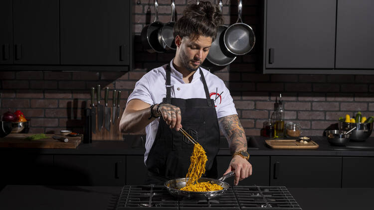 Chef Robbie Felice stands at a stove with a pan of noodles.
