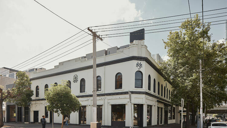 The corner of a white building with green trees infront