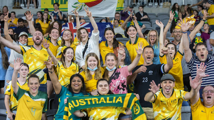 A crowd wearing green and Gold cheers on the Matildas football team.