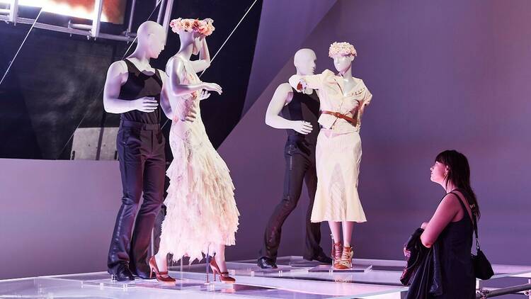 A person looks up at figures wearing dresses, posed in a partner dance position.