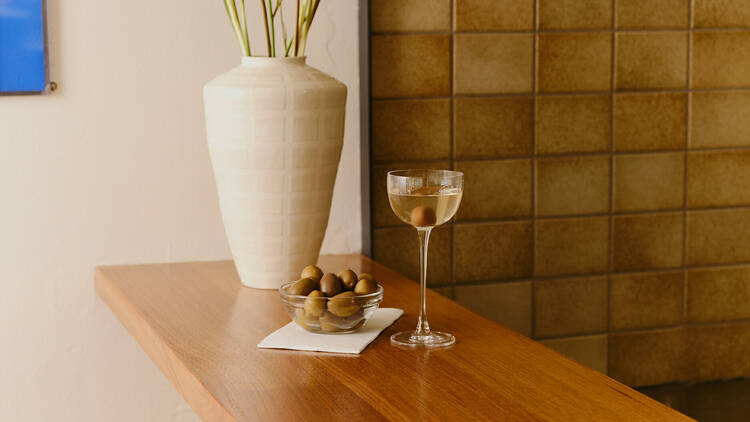 A Martini and a bowl of olives on a wooden bar.