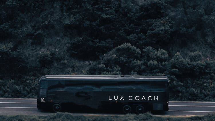 A sleek, black bus driving along a road surrounded by bushland.