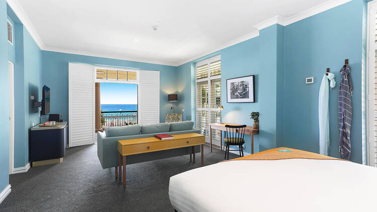 A hotel room with blue walls, a white bedspread and a view of the ocean.