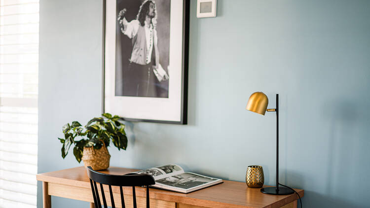 A desk with a gold and black lamp, against a blue wall with a black and white framed black and white photo of Michael Hutchence.