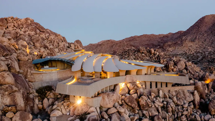 At sunset, an aerial view of the Airbnb shows its unique concrete platforms amidst the rubble of the desert hillside