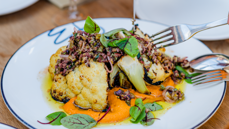 A big chunk of cauliflower on a plate with an orange-coloured sauce and herbs.