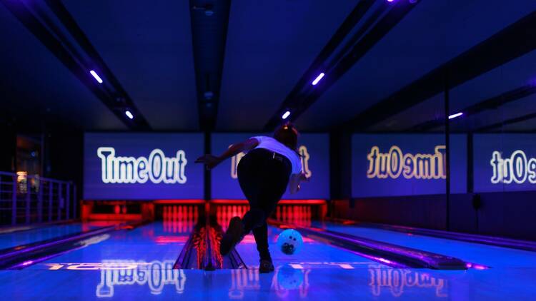 A person bowls on an illuminated Time Out branded lane.