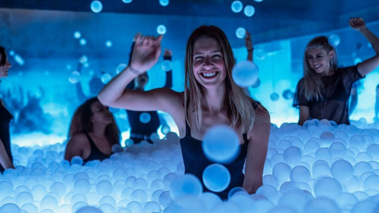 People jump in a glowing pink ball pit