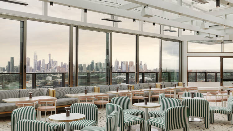 A dining space with green and white striped seating and views of Melbourne's city skyline through the windows